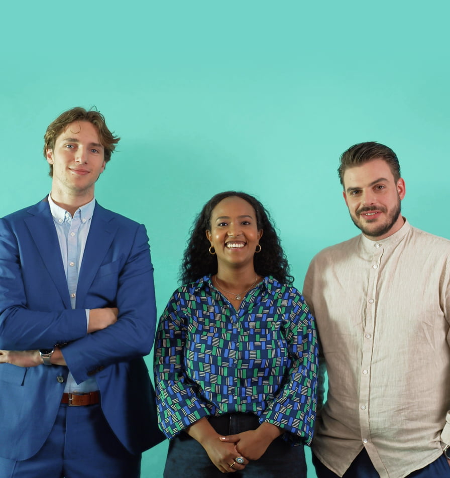 Drie mensen staan vriendelijk lachend voor een blauwgroene achtergrond. Links en rechts staan twee mannen, en in het midden een vrouw.